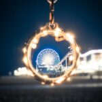 Beverly Hills Magazine 6 LA Restaurants With An Ocean View. View of Santa Monica Pier at night from the beach, shot through a decorative keychain.